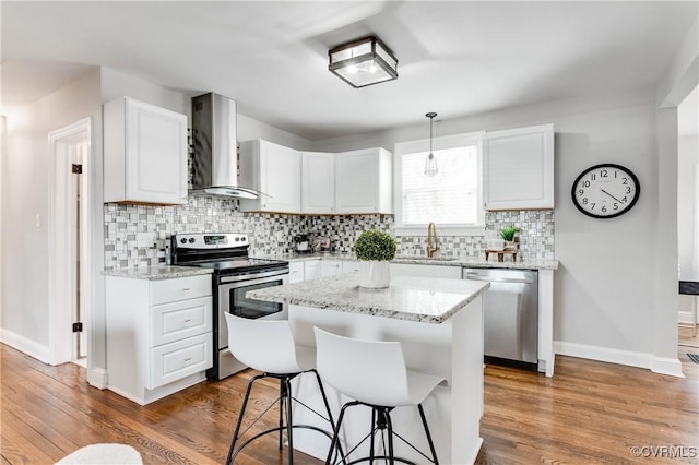 kitchen with appliances with stainless steel finishes, pendant lighting, white cabinetry, and wall chimney exhaust hood