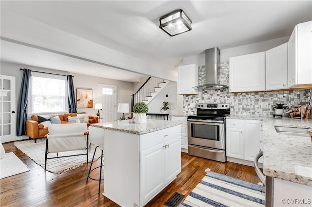 kitchen with a center island, electric stove, open floor plan, white cabinets, and wall chimney range hood