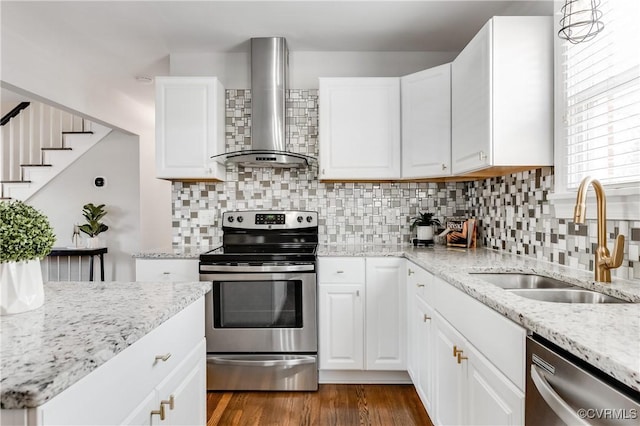 kitchen with wall chimney exhaust hood, white cabinetry, stainless steel appliances, and a sink