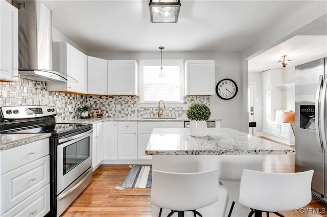 kitchen featuring stainless steel appliances, a sink, white cabinetry, wall chimney range hood, and decorative light fixtures