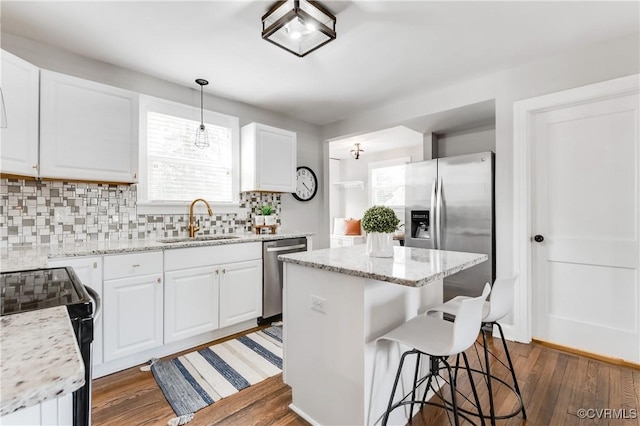 kitchen with stainless steel appliances, a sink, white cabinets, a center island, and pendant lighting