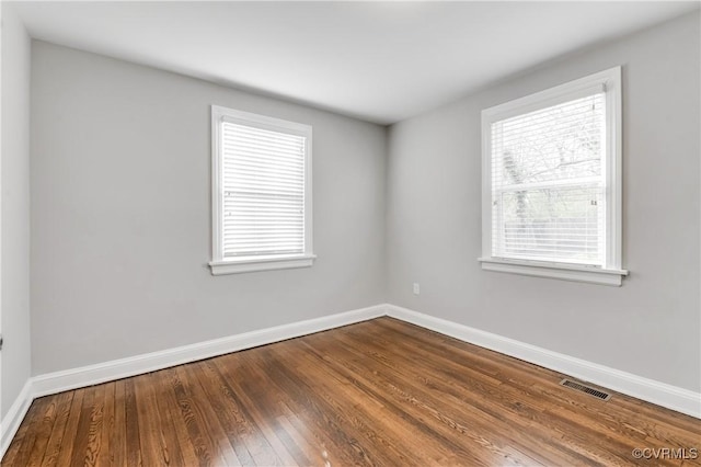 unfurnished room with wood finished floors, visible vents, and baseboards