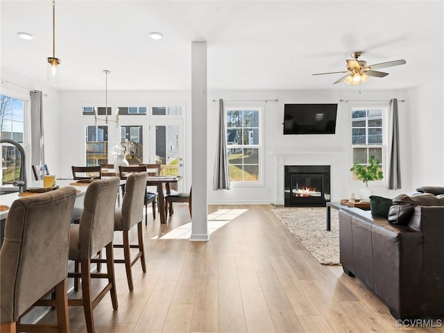 interior space with ceiling fan, baseboards, a fireplace with flush hearth, and light wood-style floors