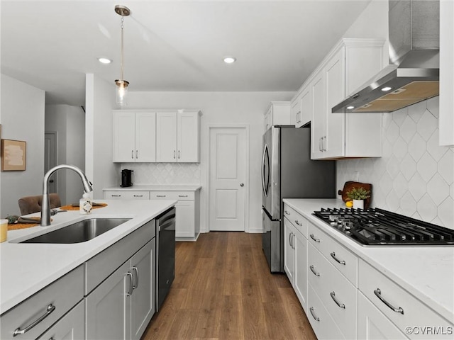 kitchen featuring light countertops, a sink, wall chimney range hood, and white cabinetry