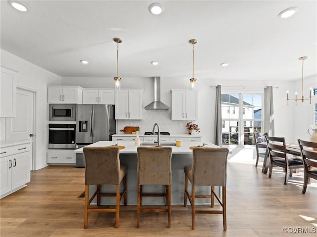 kitchen with white cabinets, light countertops, appliances with stainless steel finishes, wall chimney exhaust hood, and decorative light fixtures