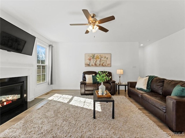 living area featuring ceiling fan, baseboards, wood finished floors, and a glass covered fireplace