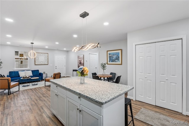 kitchen featuring a breakfast bar area, light stone counters, a center island, hanging light fixtures, and hardwood / wood-style floors