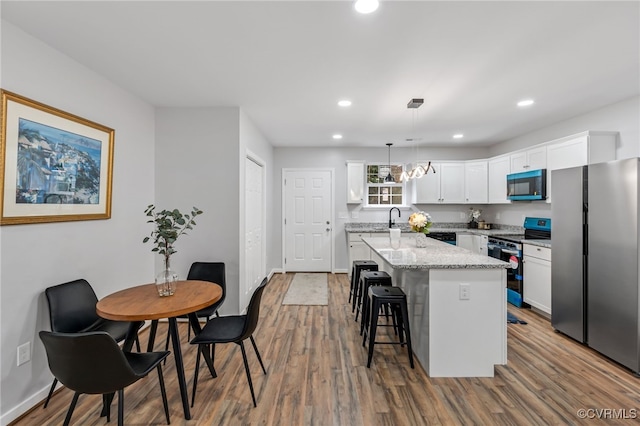 kitchen with a kitchen island, appliances with stainless steel finishes, hardwood / wood-style floors, decorative light fixtures, and white cabinetry