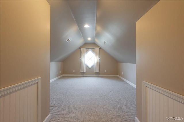 additional living space with baseboards, visible vents, vaulted ceiling, and light colored carpet