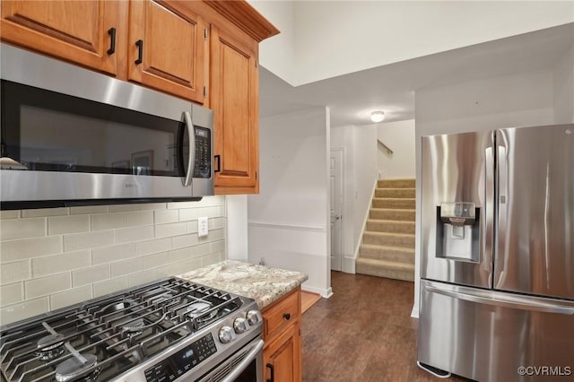 kitchen with appliances with stainless steel finishes, tasteful backsplash, light stone countertops, and dark hardwood / wood-style flooring