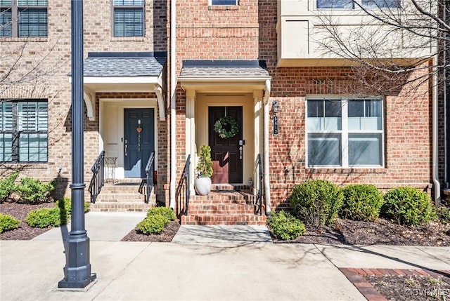 doorway to property with a shingled roof and brick siding