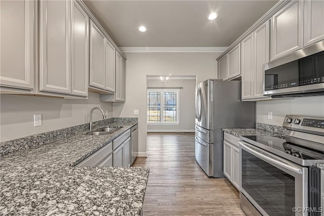 kitchen featuring crown molding, light wood-type flooring, dark stone countertops, stainless steel appliances, and a sink