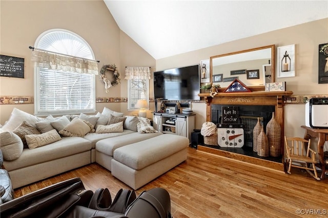 living room featuring high vaulted ceiling, a glass covered fireplace, and light wood-style flooring