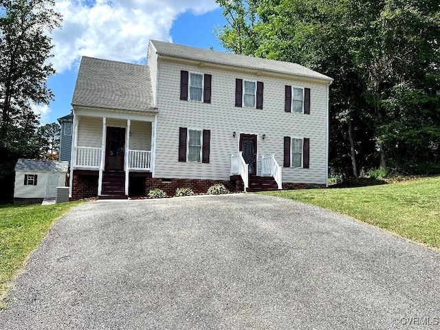 colonial home with aphalt driveway, covered porch, a front yard, and cooling unit