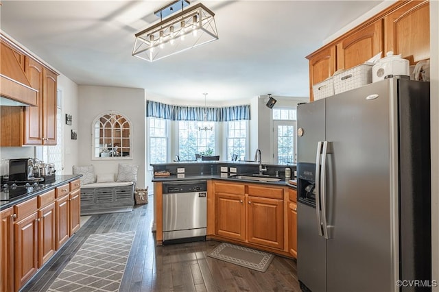 kitchen with dark countertops, appliances with stainless steel finishes, brown cabinetry, a sink, and a peninsula