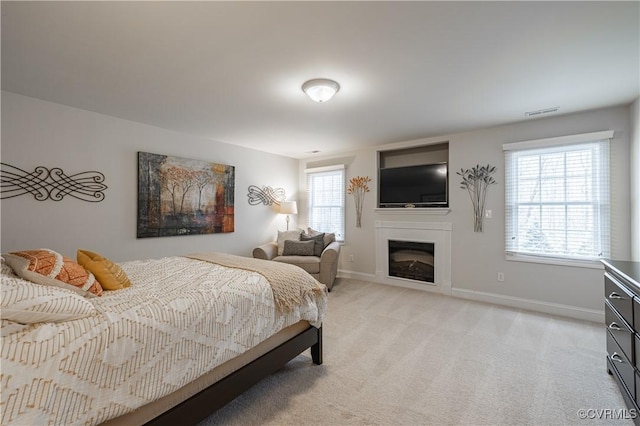 bedroom featuring light carpet, visible vents, baseboards, and a glass covered fireplace