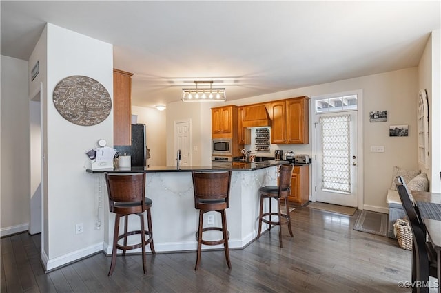 kitchen with freestanding refrigerator, stainless steel microwave, dark wood finished floors, and a kitchen bar