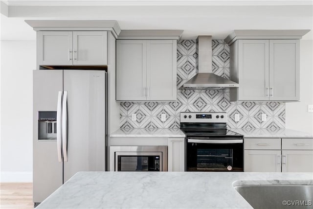 kitchen with stainless steel appliances, light stone countertops, wall chimney range hood, and tasteful backsplash