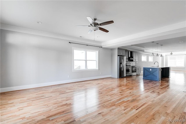 unfurnished living room with ornamental molding, a wealth of natural light, a sink, and light wood-style flooring