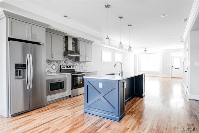 kitchen featuring stainless steel appliances, a sink, light countertops, wall chimney exhaust hood, and an island with sink