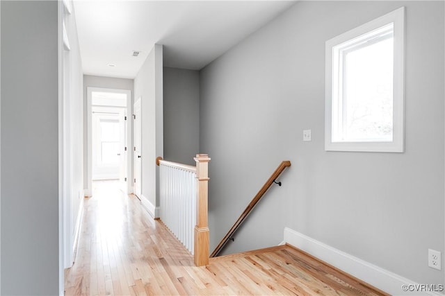 corridor with light wood-style flooring, baseboards, and an upstairs landing