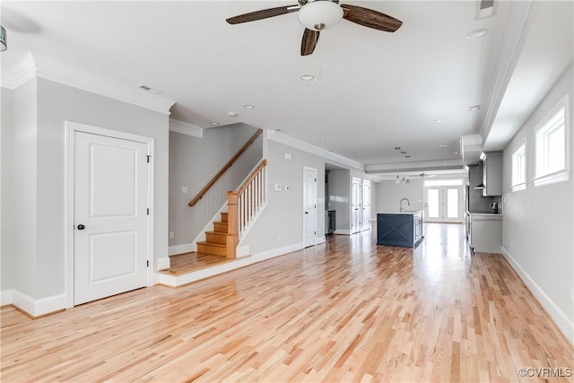 unfurnished living room featuring light wood-type flooring, stairs, ornamental molding, and a sink