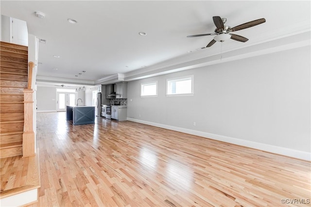 unfurnished living room featuring light wood-style flooring, stairs, baseboards, and a wealth of natural light