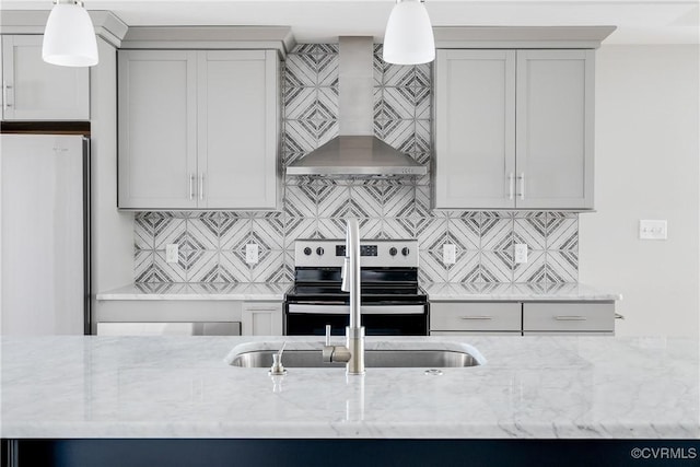 kitchen with electric range, tasteful backsplash, freestanding refrigerator, light stone countertops, and wall chimney range hood