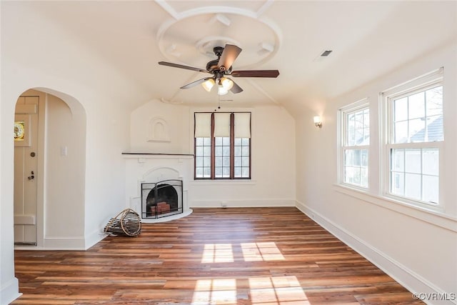 unfurnished living room featuring baseboards, arched walkways, ceiling fan, wood finished floors, and a fireplace