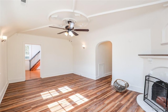 unfurnished living room featuring arched walkways, a fireplace, a ceiling fan, wood finished floors, and baseboards