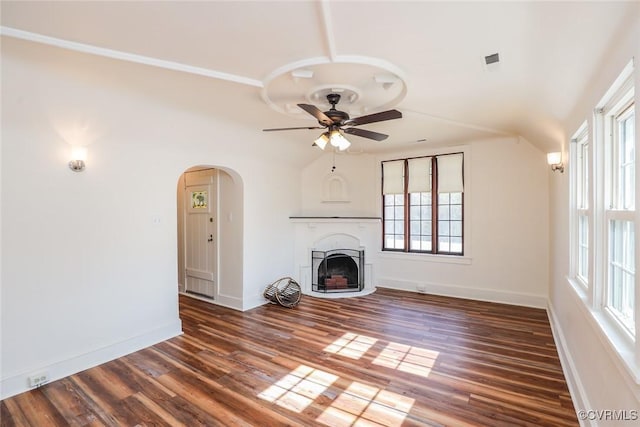 unfurnished living room featuring dark wood-type flooring, arched walkways, a fireplace, and ceiling fan