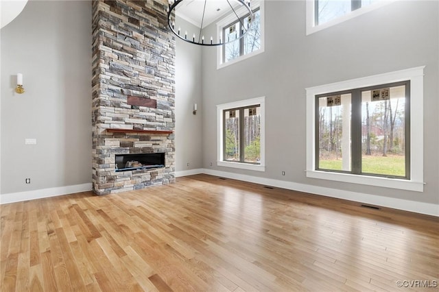 unfurnished living room with a fireplace, a high ceiling, wood finished floors, a chandelier, and baseboards