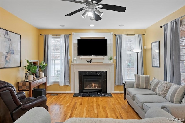 living room featuring a high end fireplace, ceiling fan, and wood-type flooring