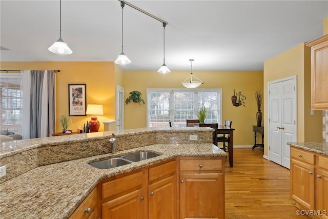 kitchen with sink, pendant lighting, light stone countertops, and light wood-type flooring