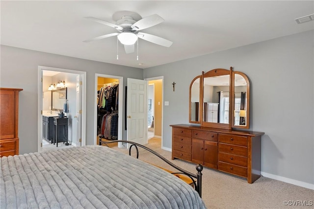 bedroom featuring light colored carpet, a walk in closet, ensuite bath, a closet, and ceiling fan