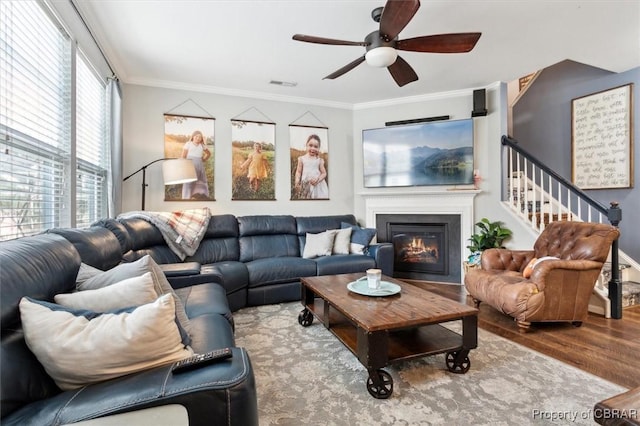 living area featuring visible vents, a glass covered fireplace, crown molding, and wood finished floors