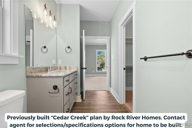 bathroom featuring a spacious closet, toilet, vanity, wood finished floors, and baseboards