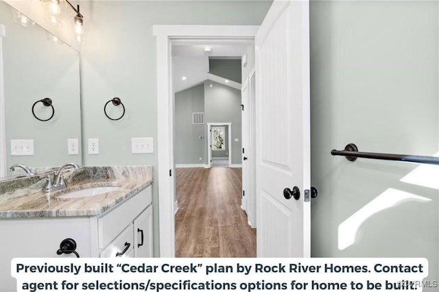 bathroom featuring visible vents, vaulted ceiling, vanity, wood finished floors, and baseboards