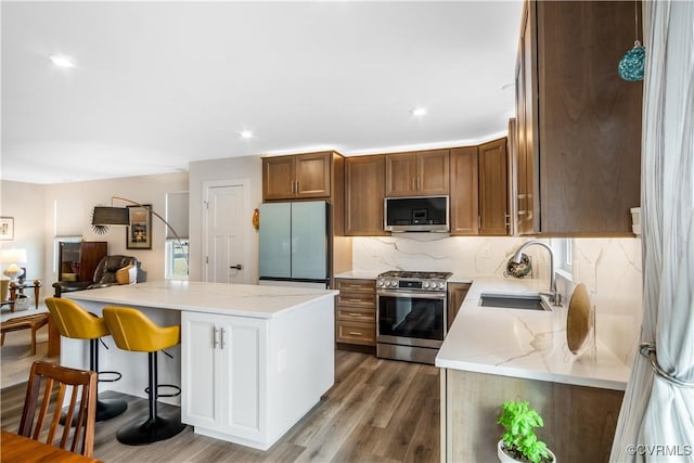 kitchen featuring decorative backsplash, wood finished floors, light stone countertops, a sink, and stainless steel appliances