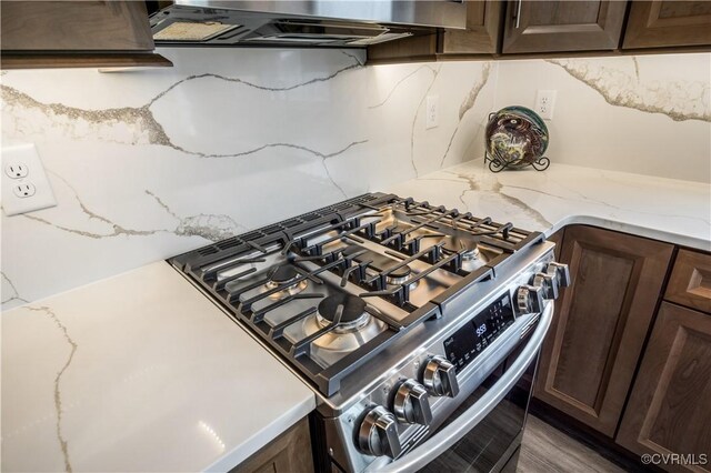 interior details featuring decorative backsplash, dark brown cabinets, gas stove, light stone counters, and under cabinet range hood