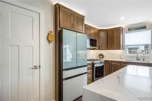 kitchen with brown cabinets, appliances with stainless steel finishes, light stone counters, a sink, and decorative backsplash