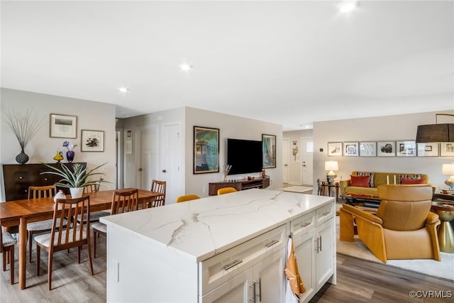 kitchen featuring light stone counters, light wood-style flooring, a center island, white cabinetry, and open floor plan