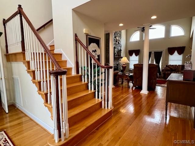 stairs featuring hardwood / wood-style flooring, ceiling fan, and decorative columns