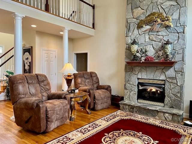 living room featuring ornate columns, a towering ceiling, hardwood / wood-style floors, and a fireplace