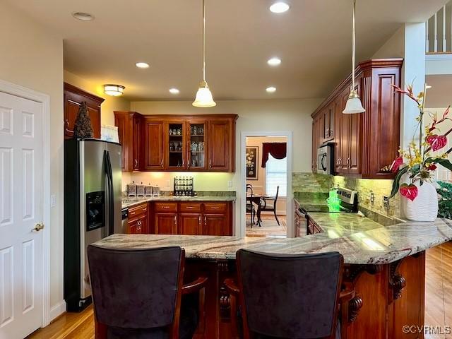 kitchen featuring light stone countertops, decorative light fixtures, stainless steel appliances, and kitchen peninsula