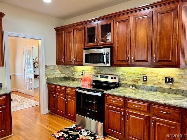 kitchen featuring light stone countertops, backsplash, light hardwood / wood-style flooring, and stainless steel appliances