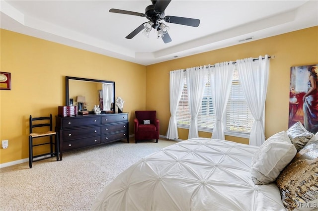 carpeted bedroom with ceiling fan and a tray ceiling