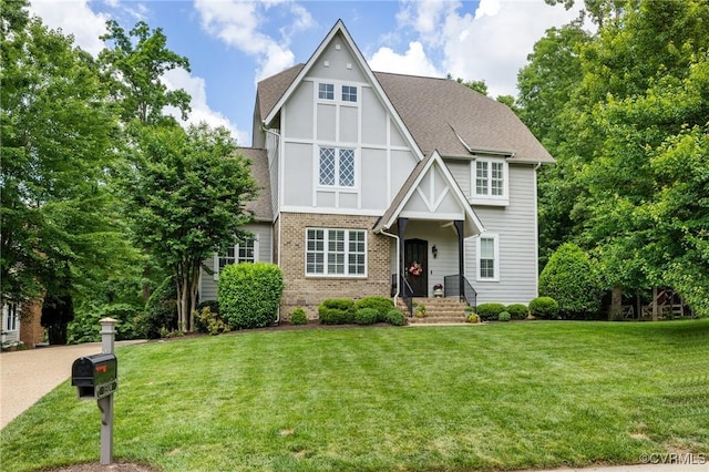 tudor home with a front yard, brick siding, and roof with shingles