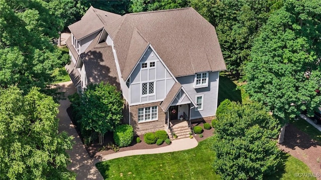 view of front facade with roof with shingles, a front yard, a chimney, and brick siding