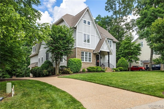 tudor home featuring brick siding, roof with shingles, and a front yard